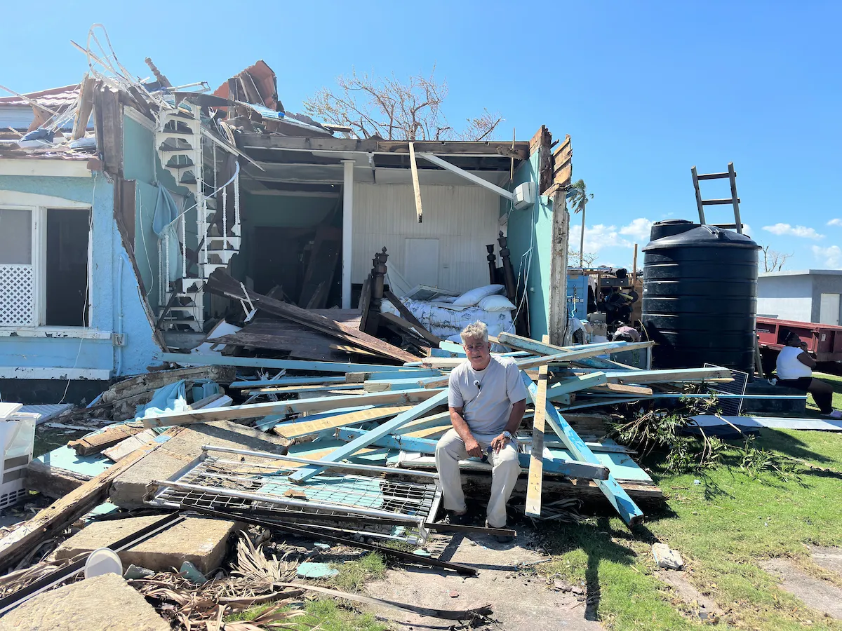 Man sits in front of destroyed house