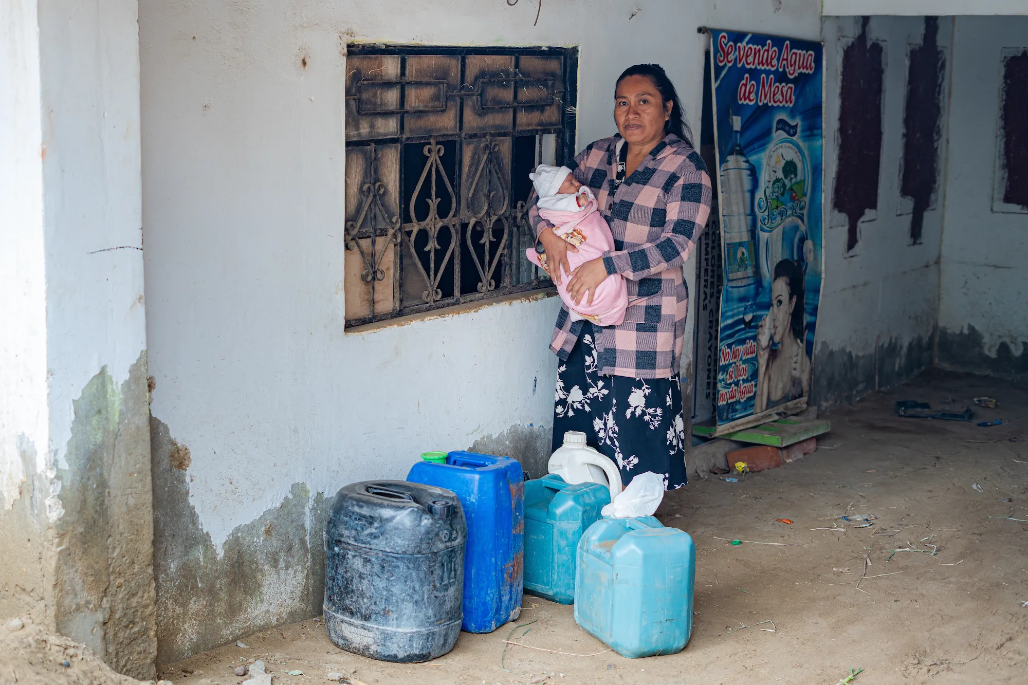 A woman and her baby stand among jerry cans