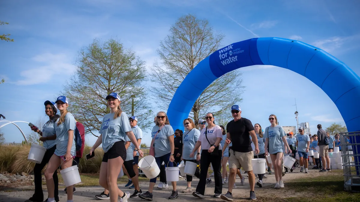 Walkers carrying buckets under Walk for Water arch