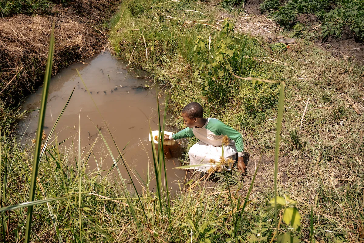 A young Ugandan girl collects dirty water from a pond