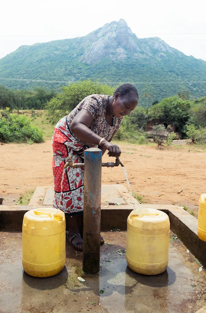 African woman gets clean water from a tap.