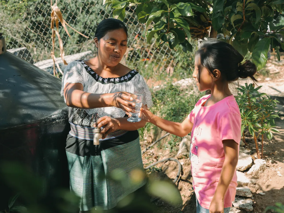 Maria hands her child a glass of water