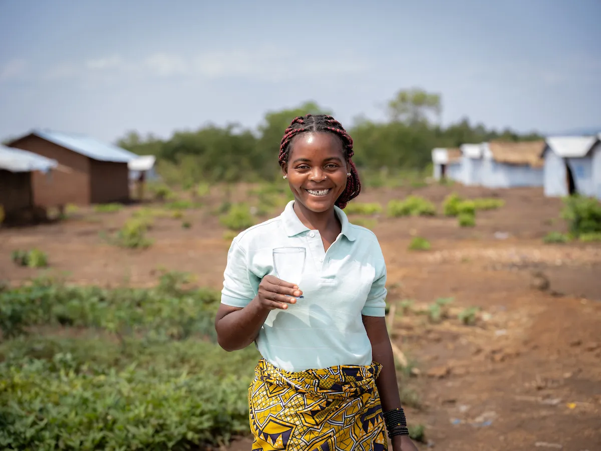 Katembo smiles with glass of safe water; Nyarugusu refugee camp; Tanzania, Africa