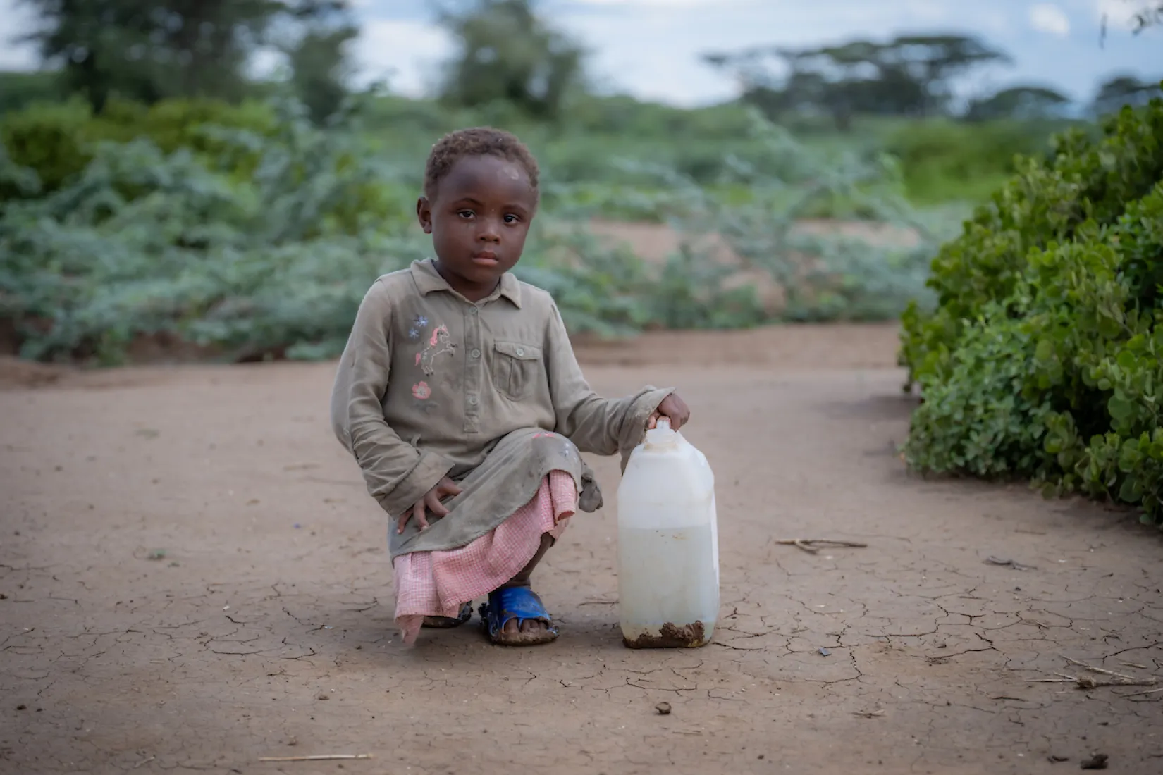 A young girl kneels next to jerry can