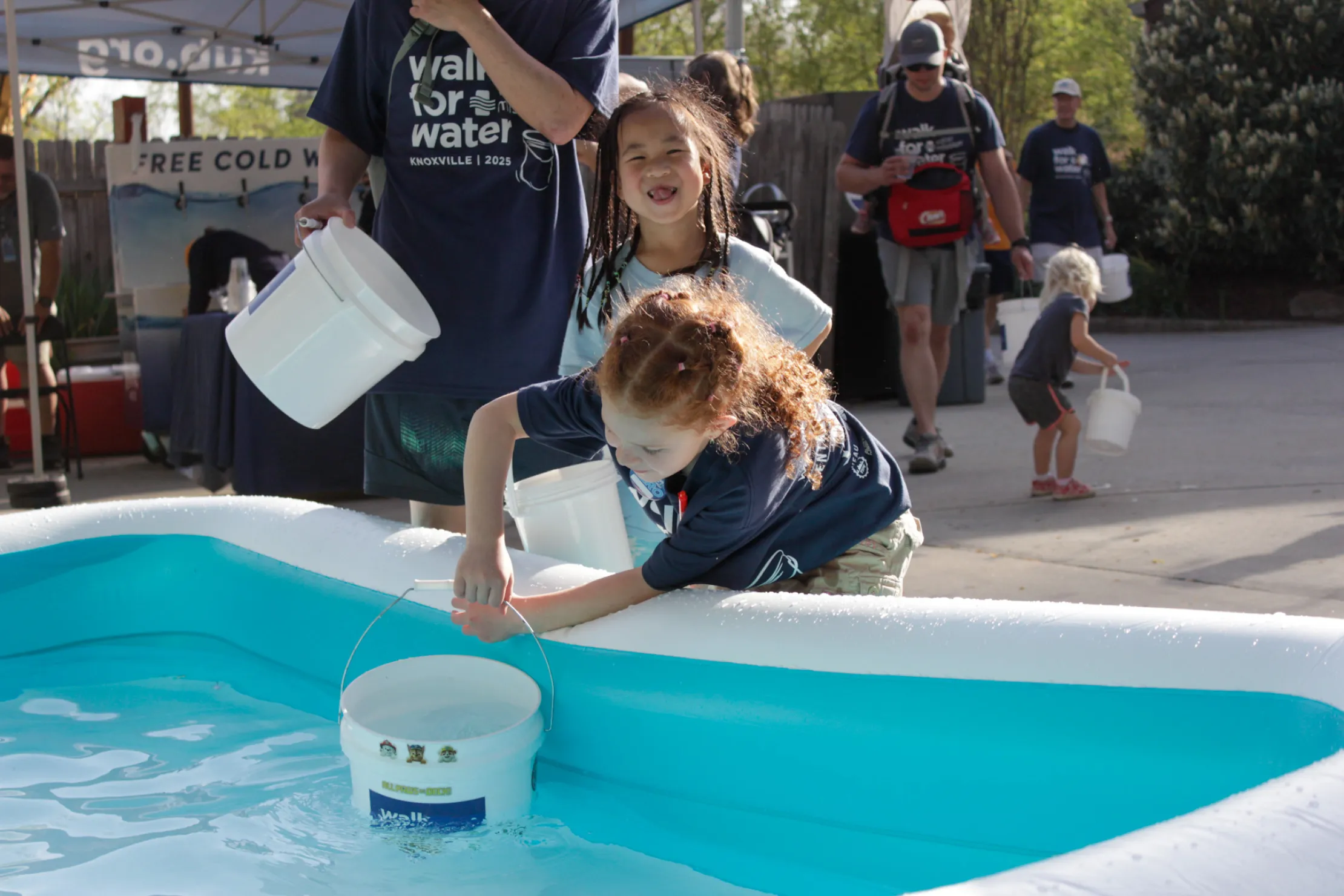 Children dip buckets into a pool of water
