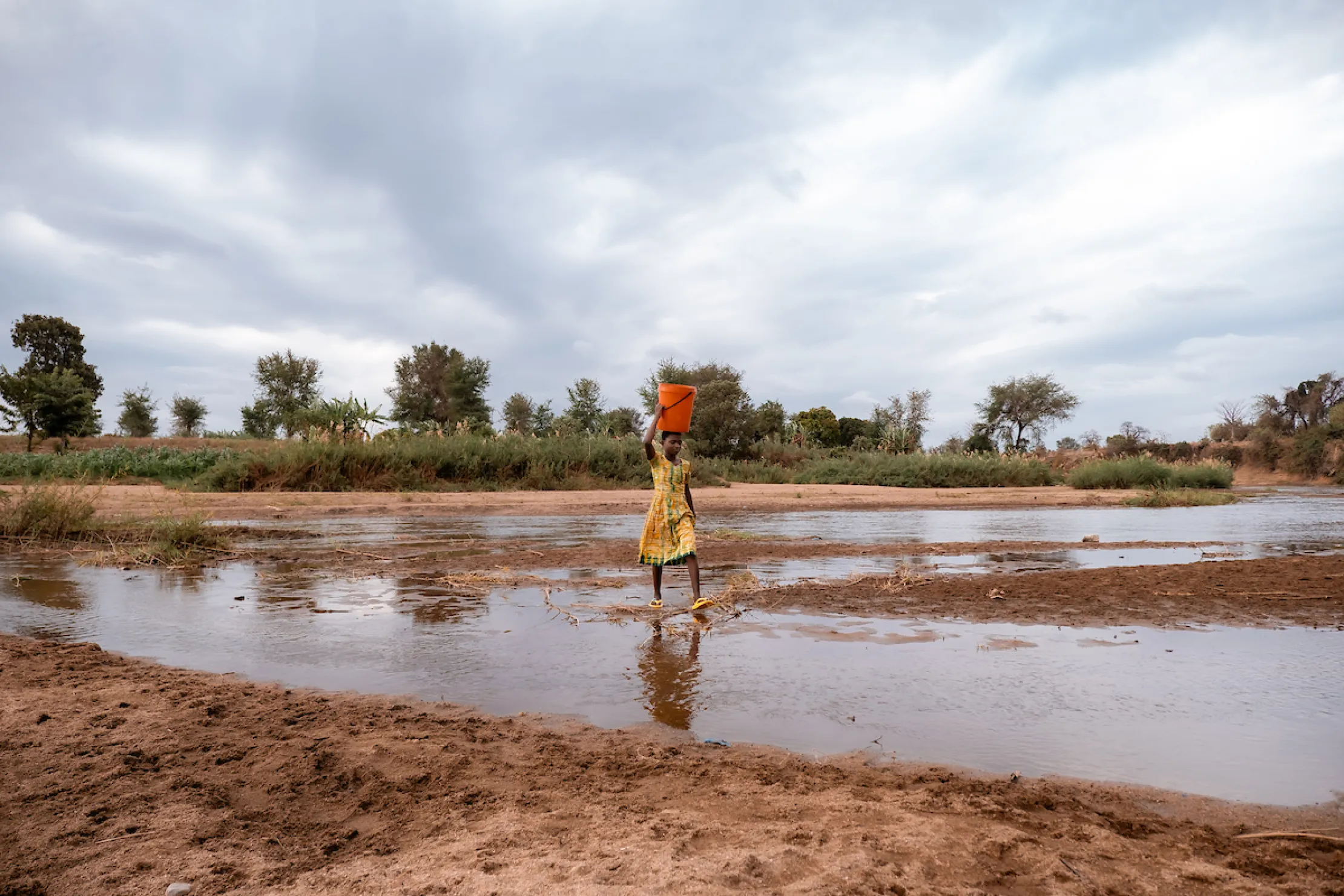 A young girl carries bucket of water on top of her head
