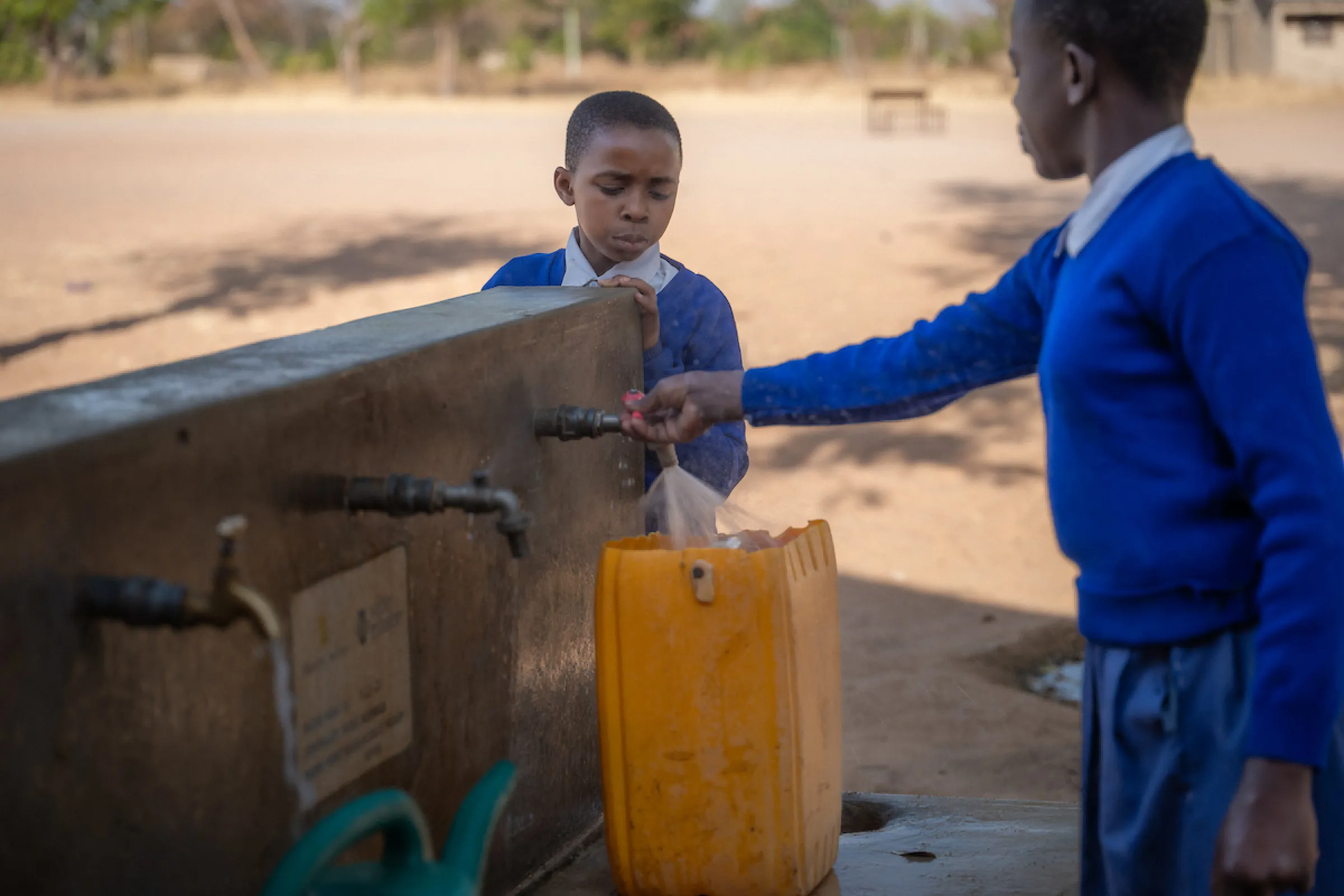 Two girls access safe water at a tap stand