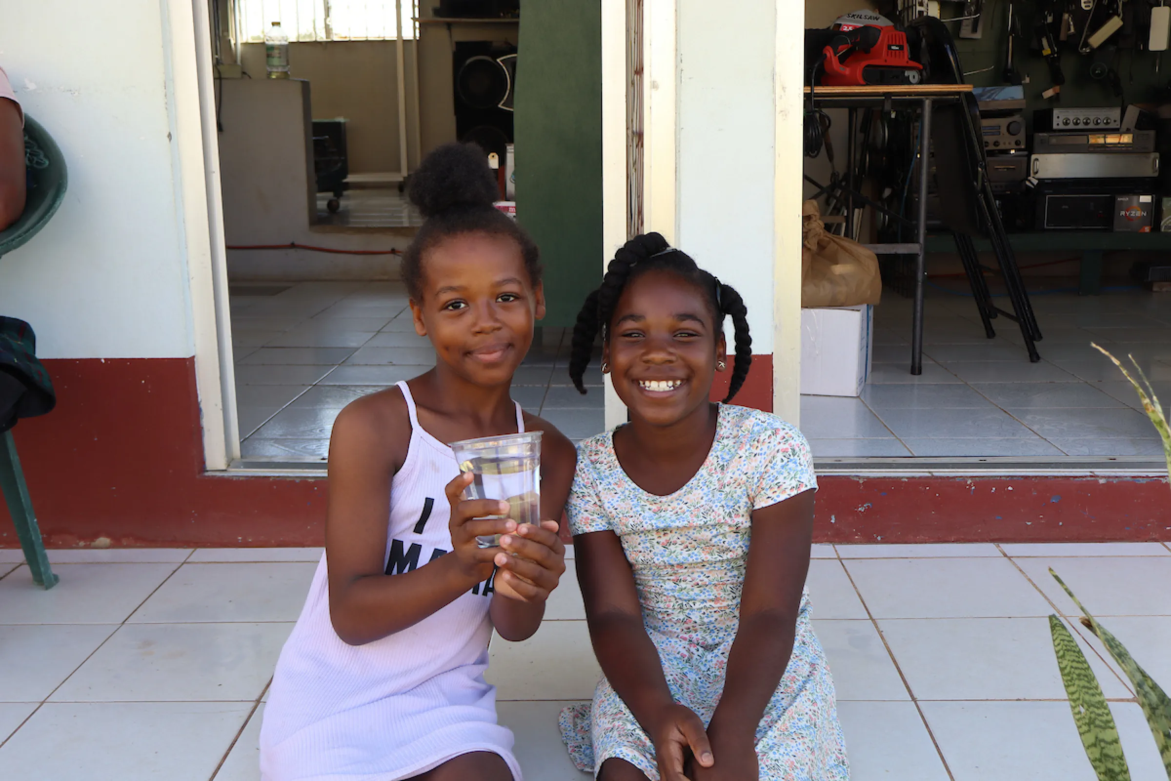 Two Jamaican girls smile while holding a glass of safe water