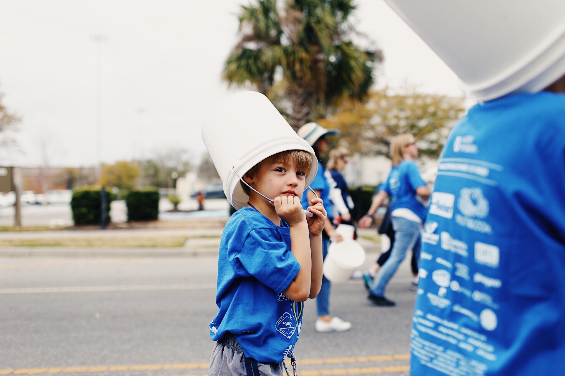 A young boy walks with his bucket on his head.