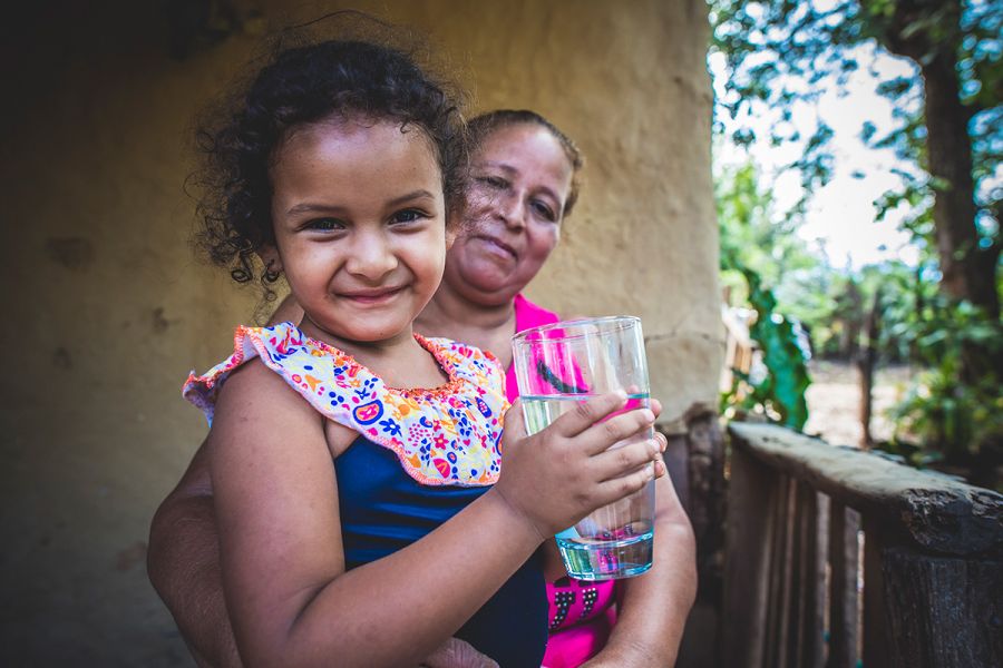 Felis holds Briyi, drinking a glass of safe water.