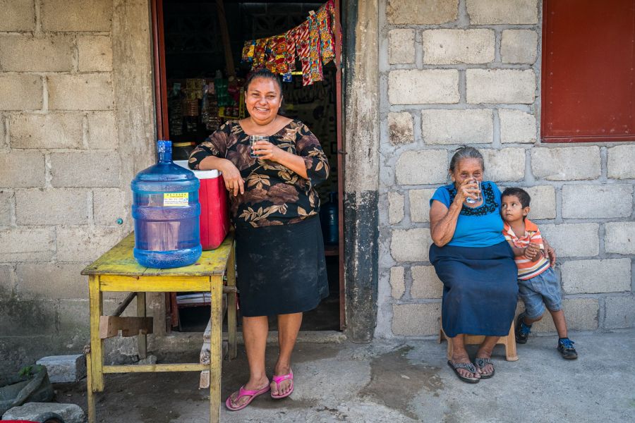 A smiling woman stands holding a glass of safe, clean water. 