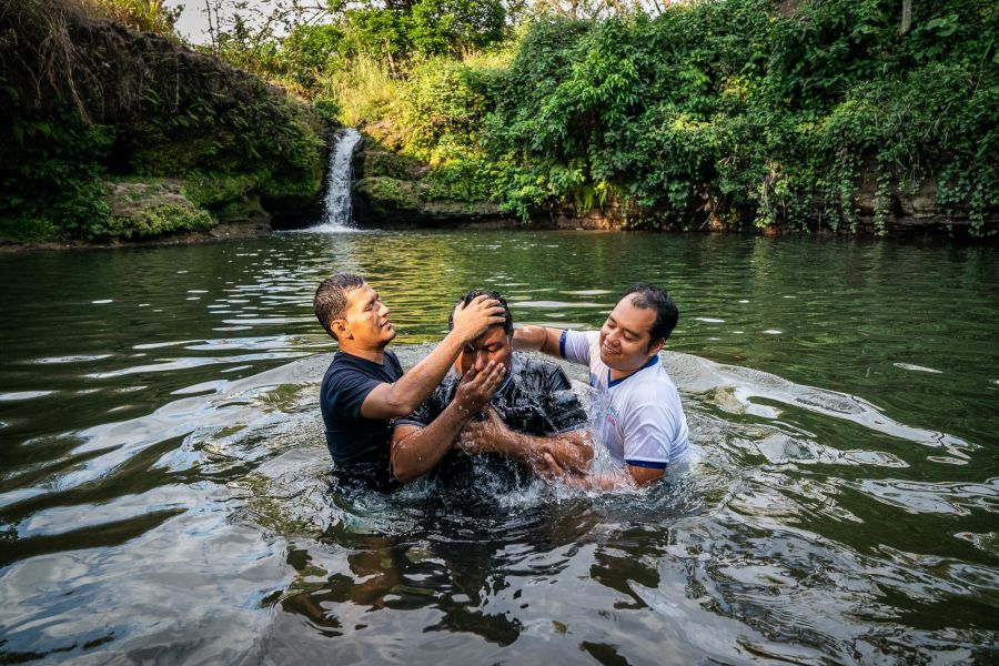 Two men help perform a water baptism for a new brother in Christ. 